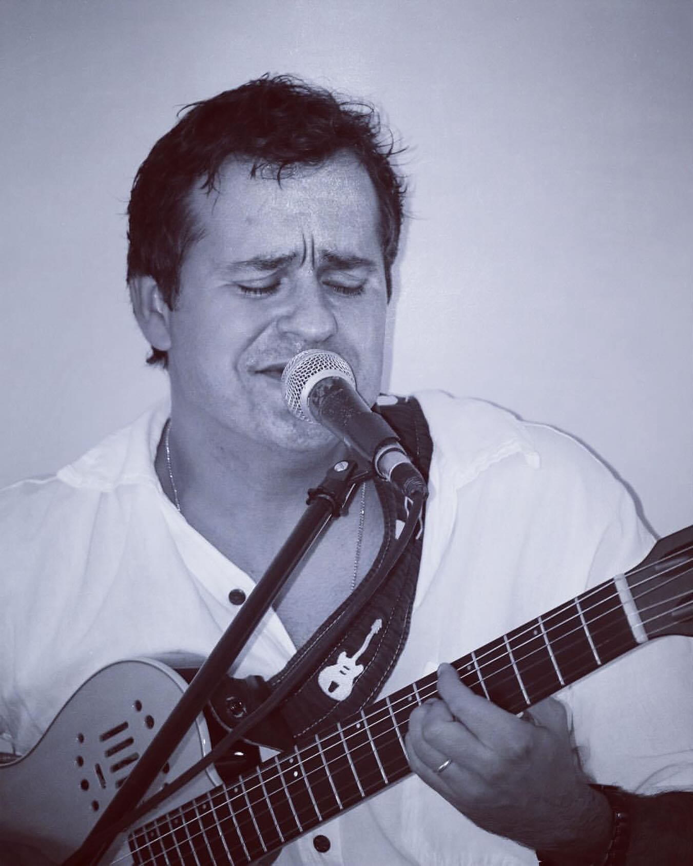 Doug Dantas singing into a microphone while playing guitar
