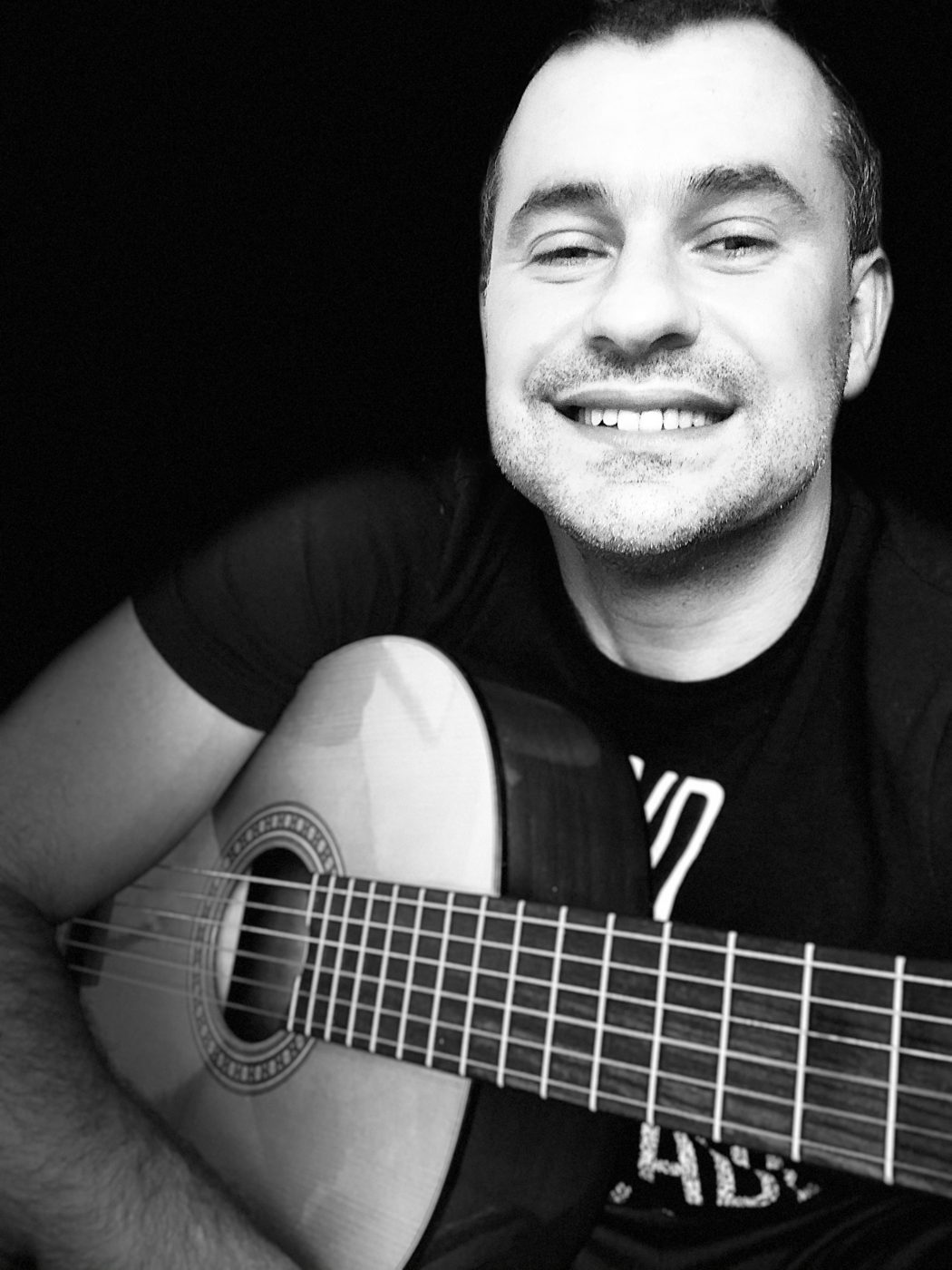 Black-and-white portrait of Doug Dantas smiling with his classical guitar